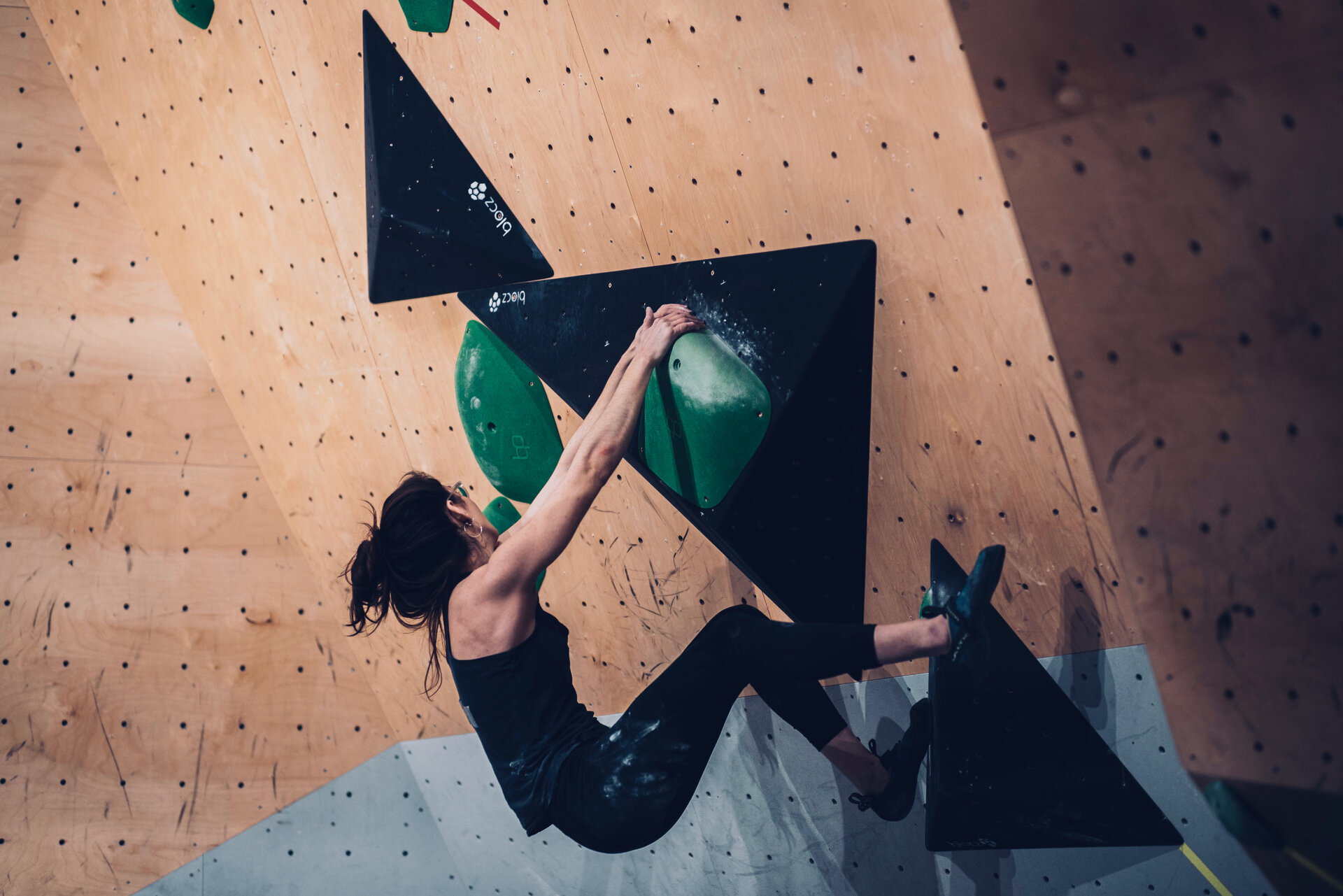 Eine Frau beim Bouldern: Sie greift mit den Händen an große grüne Griffe, während ihre Füße auf einem Volumen stehen. | © VKM